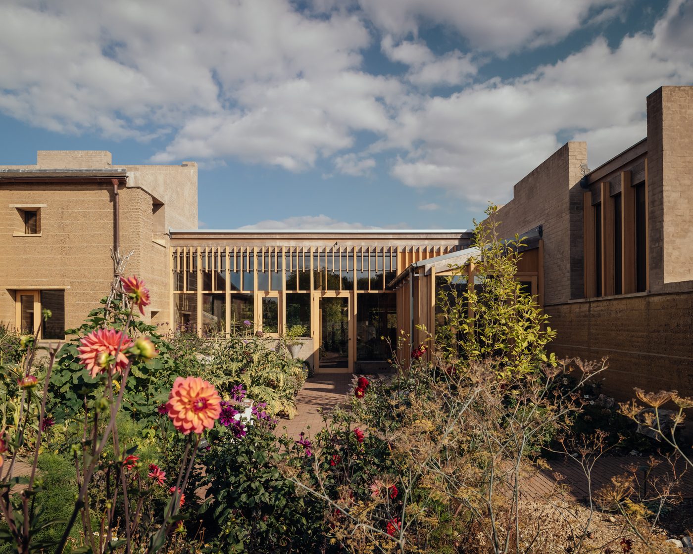 Courtyard entrance of the Rammed Earth House, Wiltshire, with timber-framed glazed frontage and dahlia garden